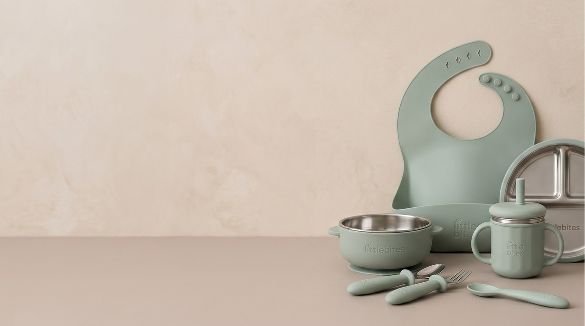 Set of green baby utensils including a bib, bowl, cup, and spoon on a beige background